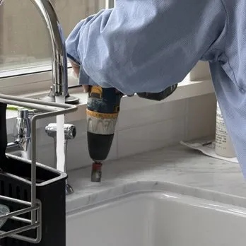 A person using a drill to install a water filtration system near a kitchen sink, representing Puronics, LLC's services in Livermore.